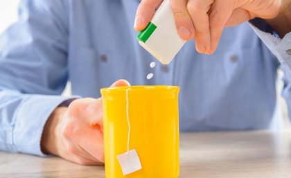 A man adds artificial sweetener tablets to a mug of tea